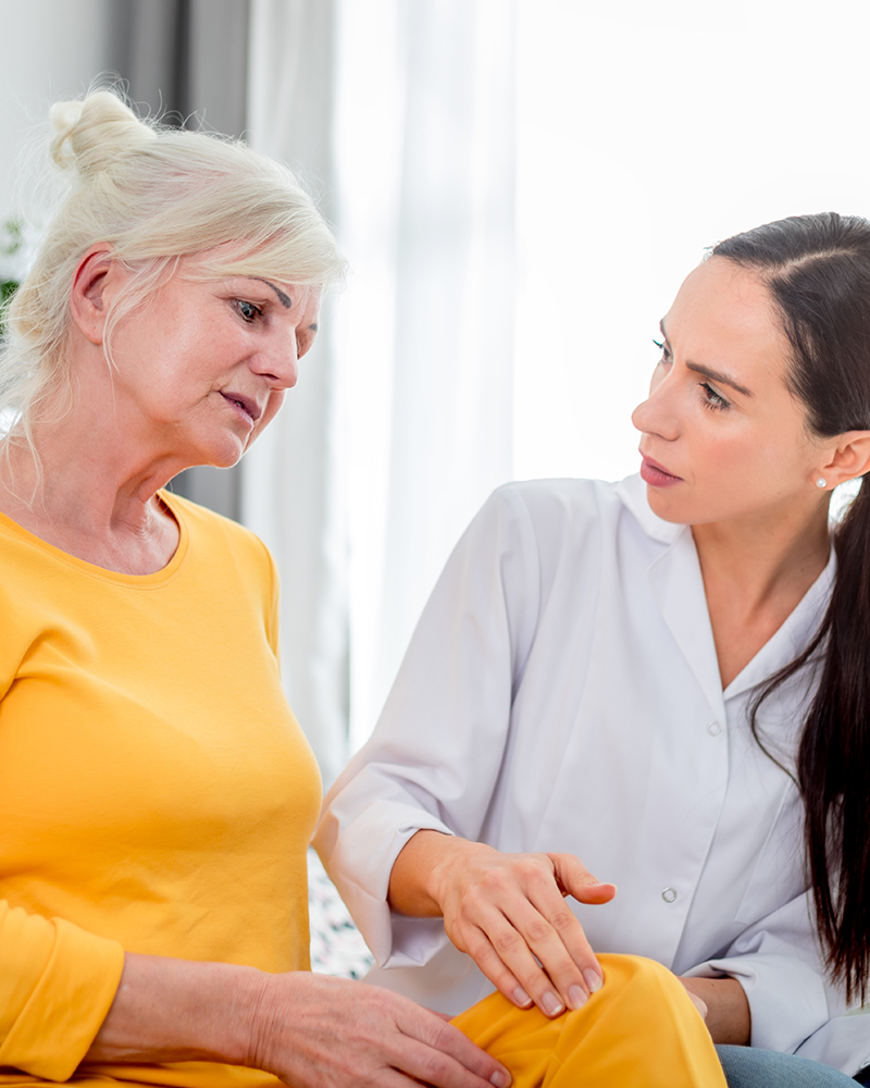 Nurse checking knee pain to senior female during home visit